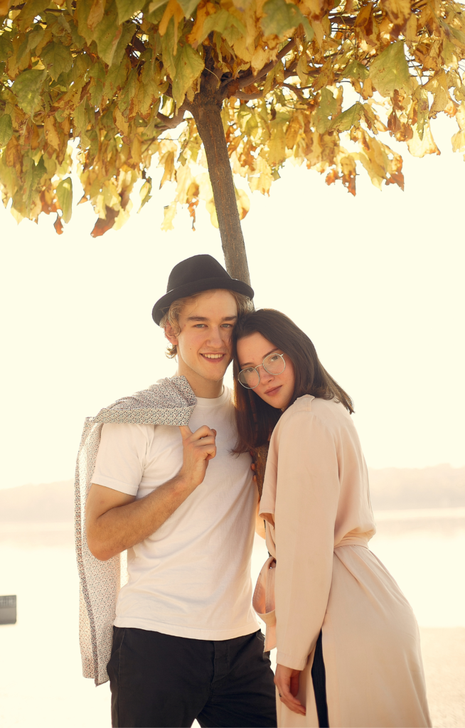 A young woman and men couple standing under tree with happy and lovely face on warm and bright light